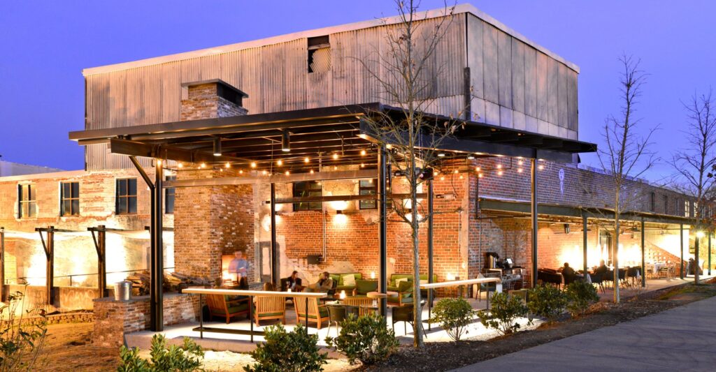 A picture capturing the inviting exterior of a steakhouse at dusk, illuminated by warm ambient lighting. The restaurant features stylish outdoor seating arrangements