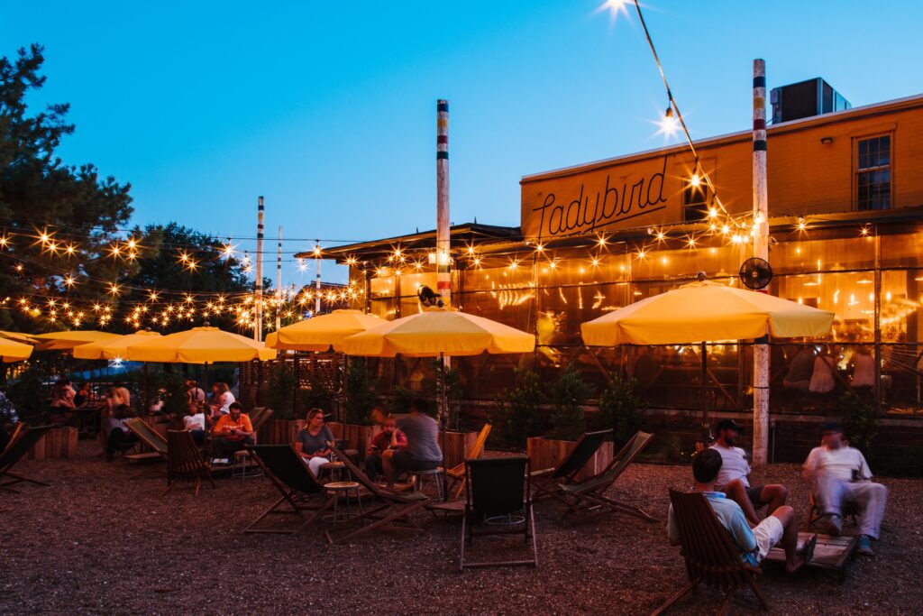A serene image of an outdoor restaurant at dusk, where relaxed seating arrangements are sheltered under soft yellow umbrellas