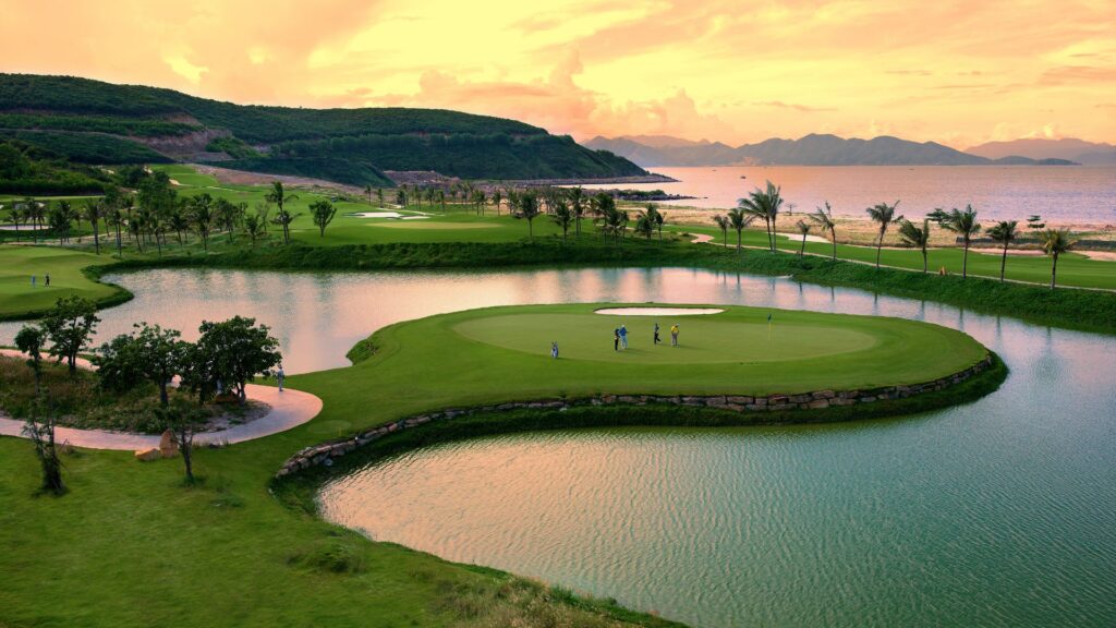 An image depicting a luxurious golf course at dusk, gracefully surrounded by shimmering bodies of water. The setting sun casts a warm glow over the meticulously maintained greens and fairways