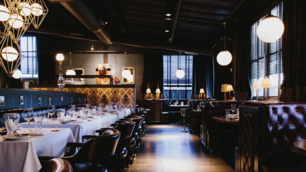 A picture taken from the inside of an elegant, high-end steakhouse, showcasing a beautiful ambiance. The interior is adorned with sophisticated decor, plush seating, and soft, warm lighting