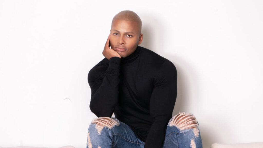 A man (Michel Smith) in a black long-sleeve shirt and blue jeans