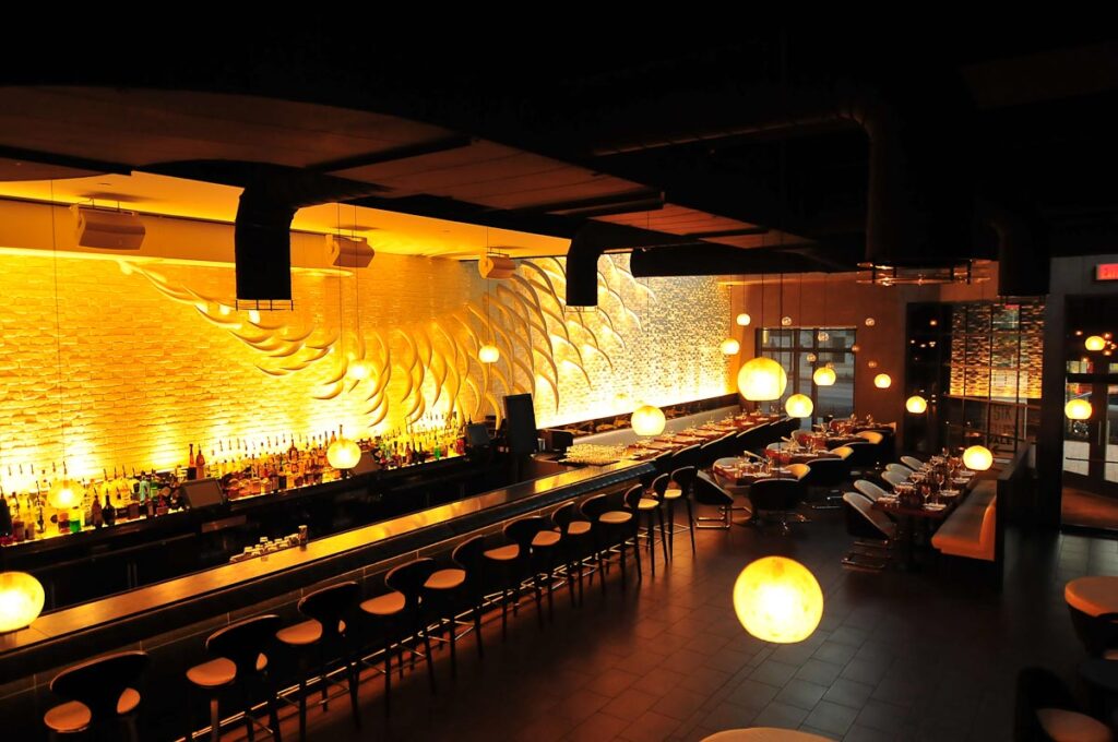 A picture showcasing the modern interior of a high-end steakhouse, bathed in a warm yellow ambiance. To the side, a beautifully lit bar stands out