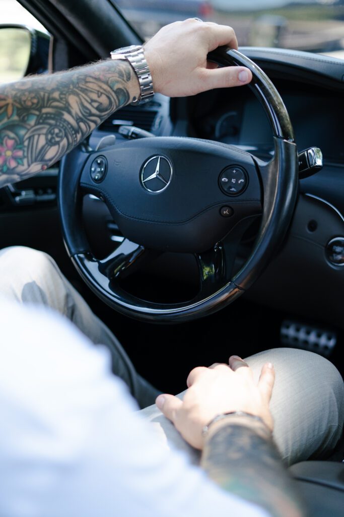 Tattooed arm gripping a Mercedes steering wheel — a statement of identity behind the wheel.