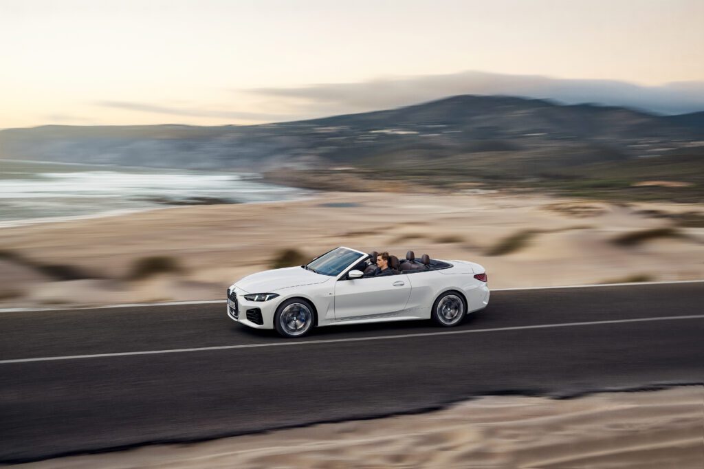 2025 BMW M440i Convertible driving along a coastal road at sunset with top down