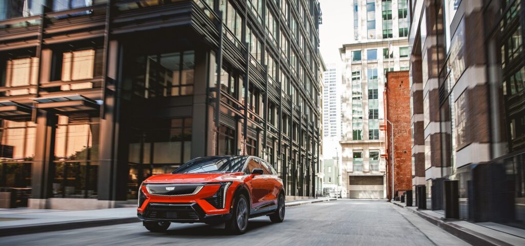 2025 Cadillac OPTIQ driving through a modern cityscape, showcasing its bold EV design and urban agility.