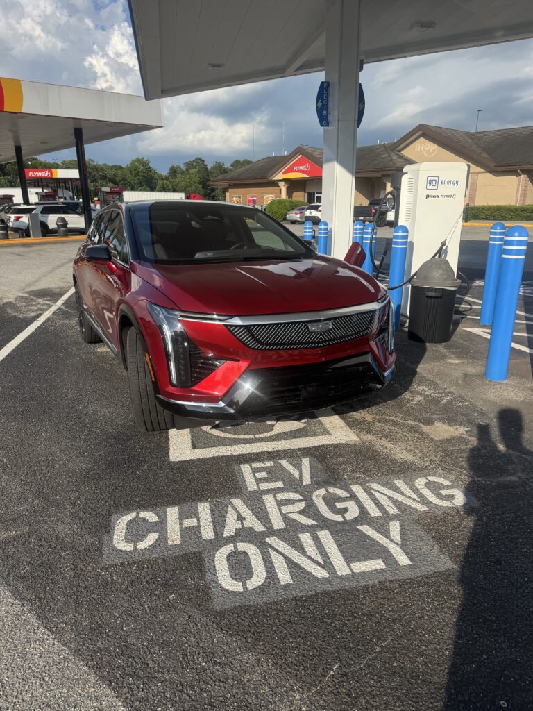 Cadillac OPTIQ parked at an EV charging station, highlighting quick-charging capability during a road trip.

