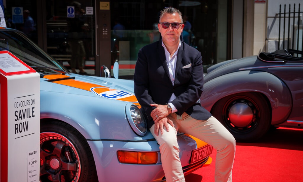 Justin Lunny, Founder & CEO of Everrati, seated on a Gulf-liveried electric Porsche 911 at the Concours on Savile Row, representing the company’s commitment to heritage-inspired electric performance.