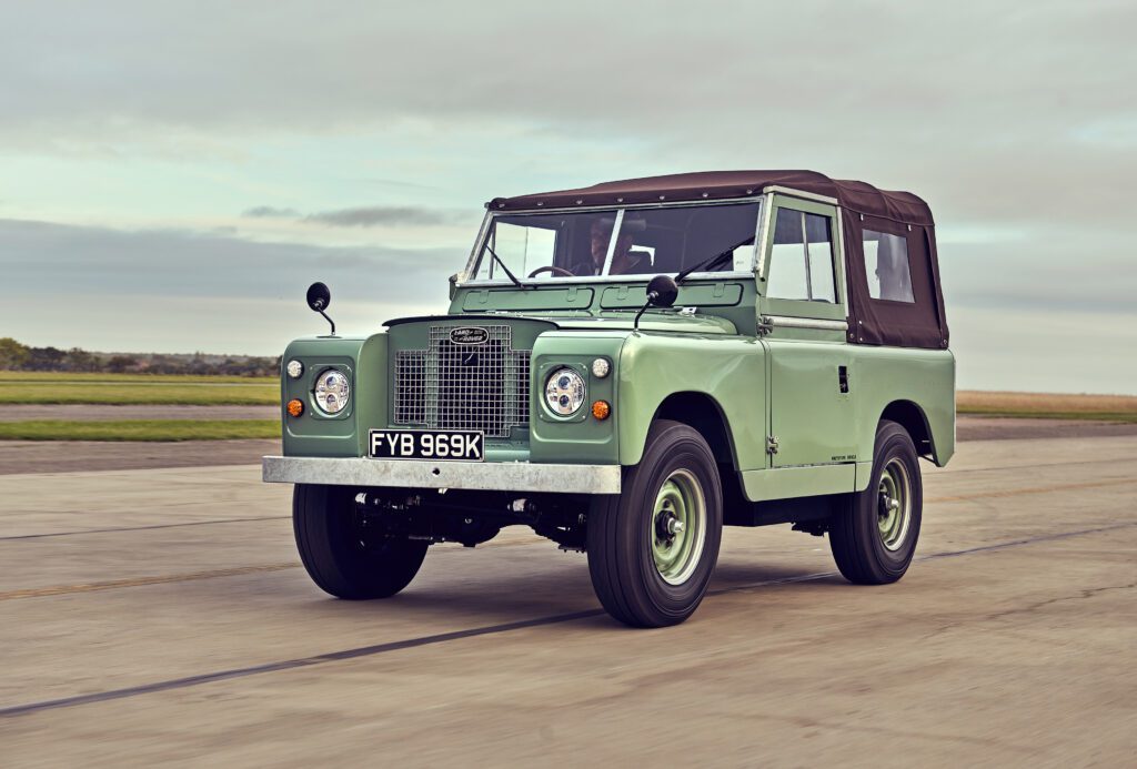 Side angle of electrified classic Land Rover Series IIA driving on a runway.