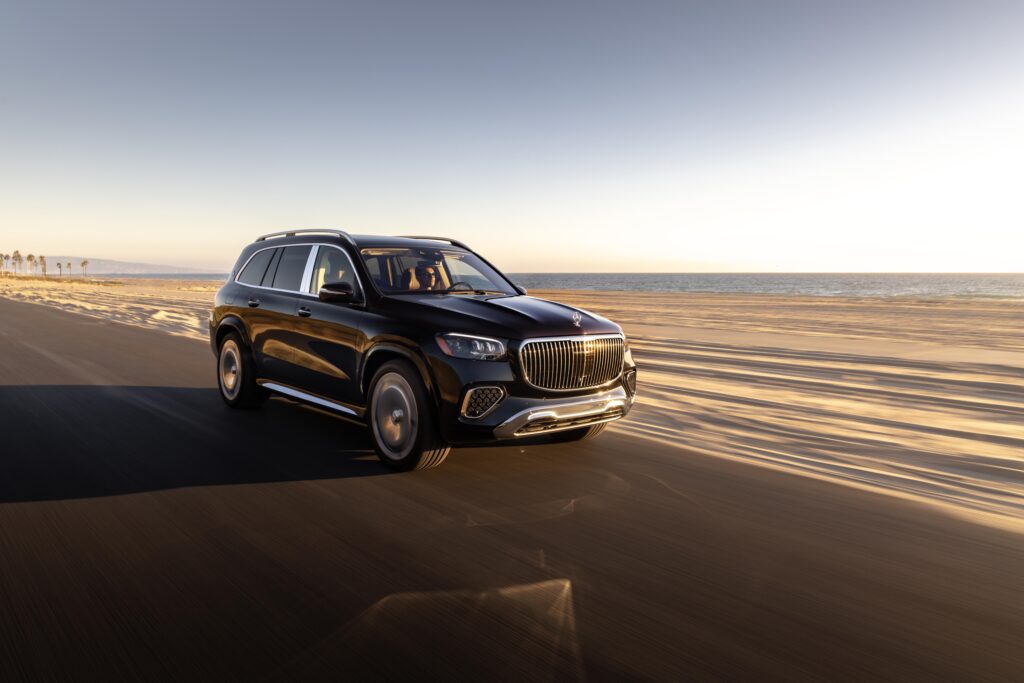Front view of the 2025 Maybach GLS luxury SUV driving along the coast at sunset.